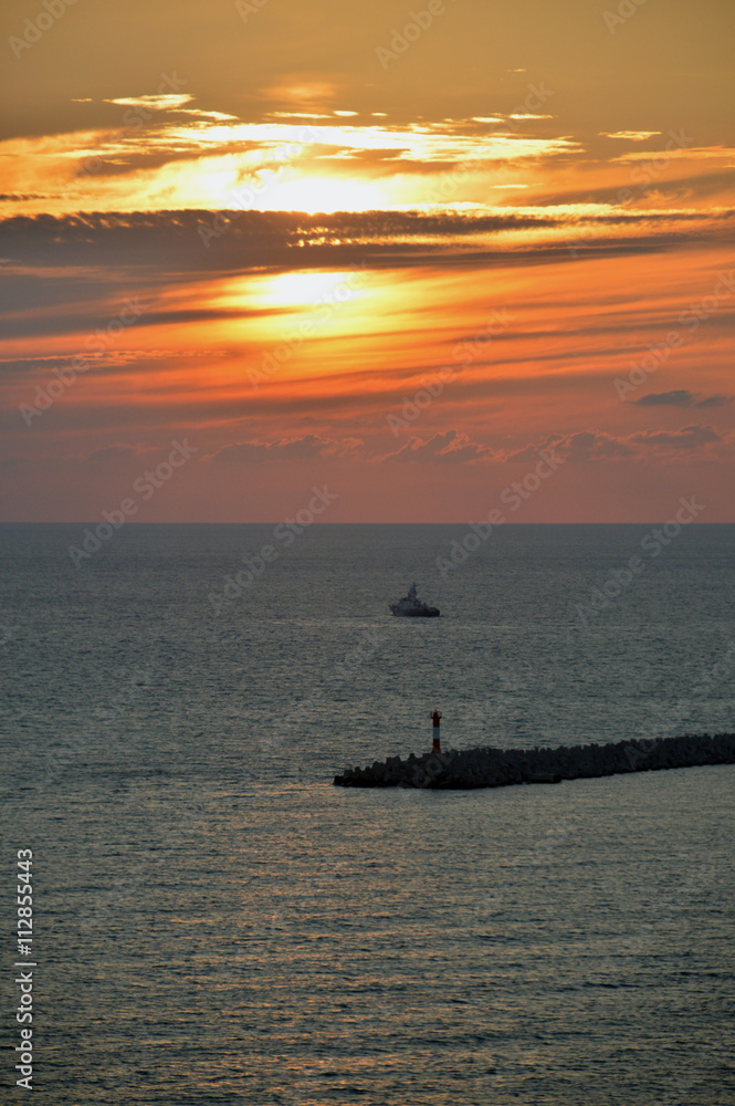 Маяк морского порта и корабль на фоне заходящего солнца