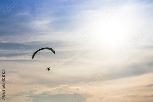 Silhouette man flying with paramotor in the blue sky