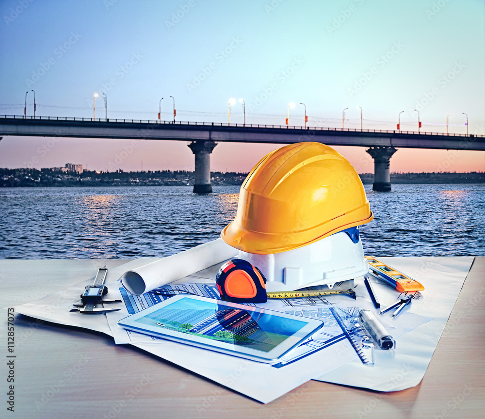 Table with construction drawings and other tools on bridge background ...