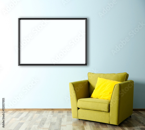 Green armchair and empty picture frame on blue wall background