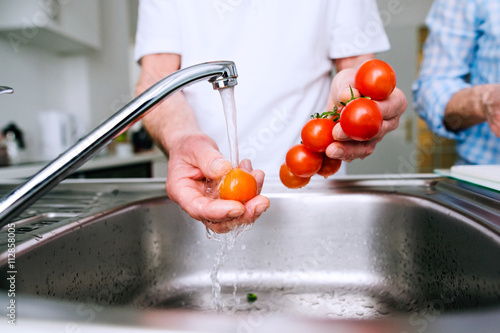 Hands of unrecognizable senior man washing tomatoes. Preparing b