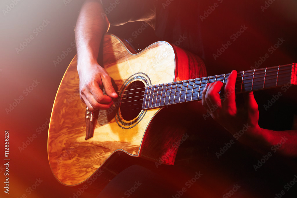 Fototapeta premium Young man playing on acoustic guitar on dark background with light effect
