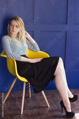 Blond girl in skirt and vest sits on a chair photo