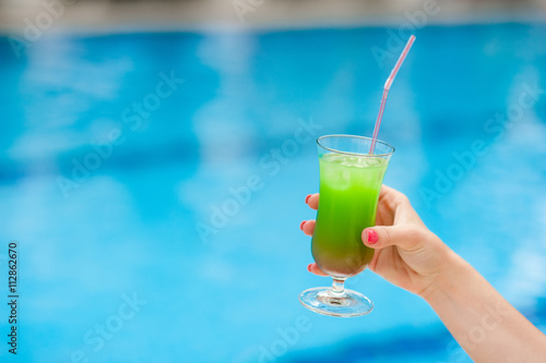 Bright cocktail in a female hand near the pool
