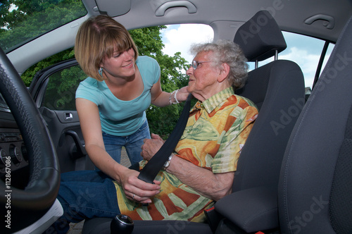 Seniorin wird von Betreuerin im Auto angeschnallt.