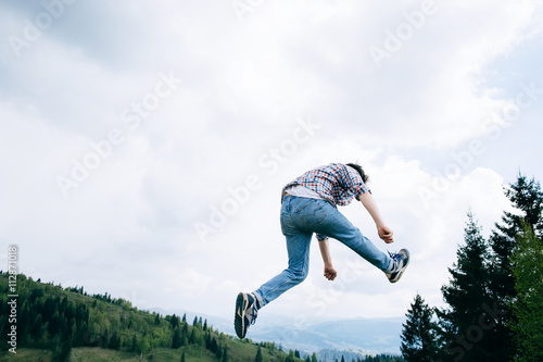 Young man Jumping Outdoors on rock in mountains sky
