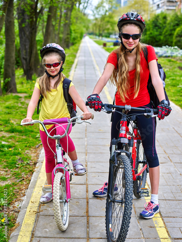 Bikes bicyclist girl. Girls wearing bicycle helmet and glass with rucksack ciclyng bicycle. Girls children cycling on yellow bike lane. Bike share program save money and time at city street. photo