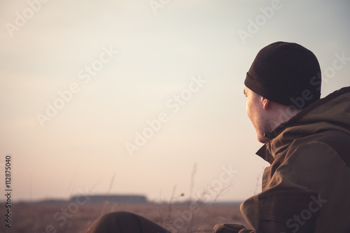 young man  looking into the distance at dawn in rural field. The light illuminates his face. Free copy space for text on the background of the morning sky © splendens