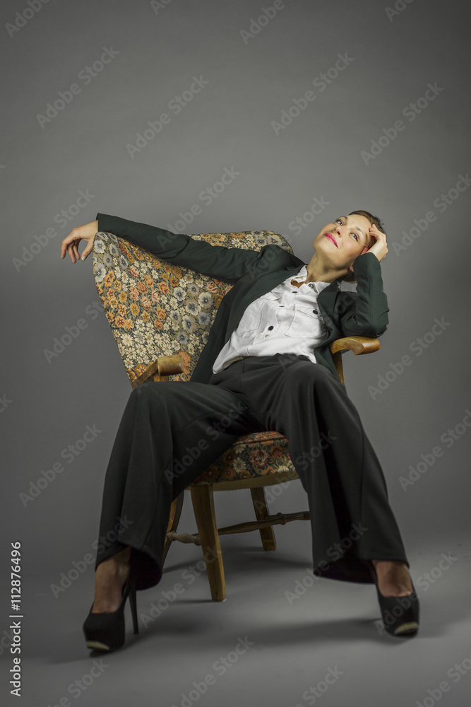 Fototapeta premium Young sensual woman in men's black suit sit in an armchair