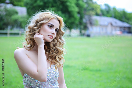 young beautiful curly blonde hair slim girl fashion portrait in white dress posing looking away calm look, in background green grass meadow. Healthy woman lifestyle concept.