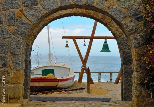 View through and arch onto the ocean outside of Pablo Nerudas house with a wooden construction with green bells and a white boat in the foreground