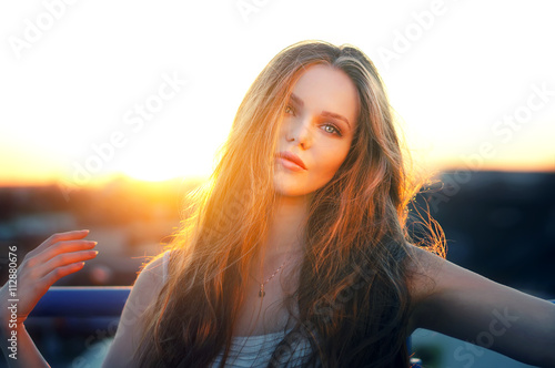 Outdoor portrait of young pretty sexy woman posing at roof at the end of bright sunset. Lovely soft back light.