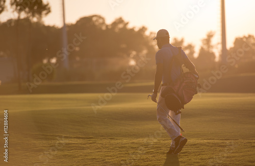 golfer walking and carrying golf bag at beautiful sunset