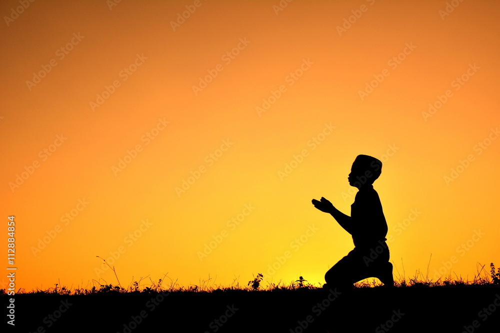 silhouette of a boy who praying over at sunset