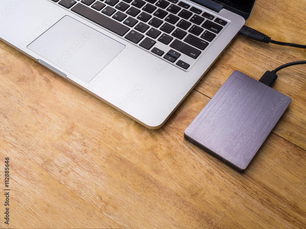 External or portable hard drive (HDD) connected to laptop computer for transfer or backup data on wooden texture office desktop with copy space External or portable hard drive (HDD) connected to laptop computer for transfer or backup data on wooden texture office desktop with copy space