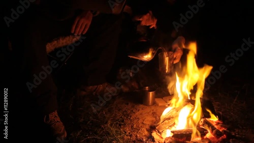 Two travelers sitting around the campfire at night poured hot tea mugs