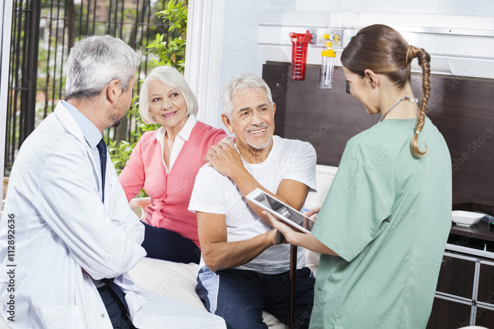 Senior Couple Looking At Female Nurse While Sitting By Doctor Senior Couple Looking At Female Nurse While Sitting By Doctor