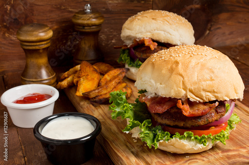 Gourmet Tasty Steak Burgers on a Wooden Tray with Potato Wedges Dipping Sauce and ketchup