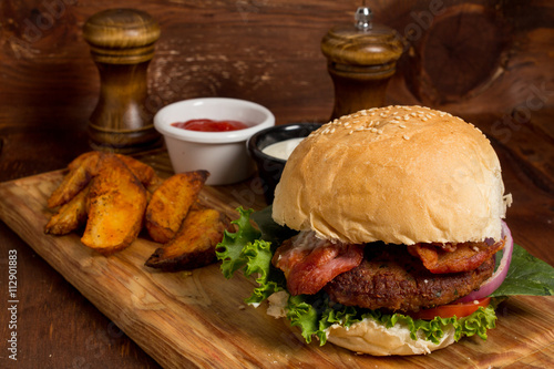 Gourmet Tasty Steak Burgers with bacon on a Wooden Tray with Potato Wedges and Dipping Sauce