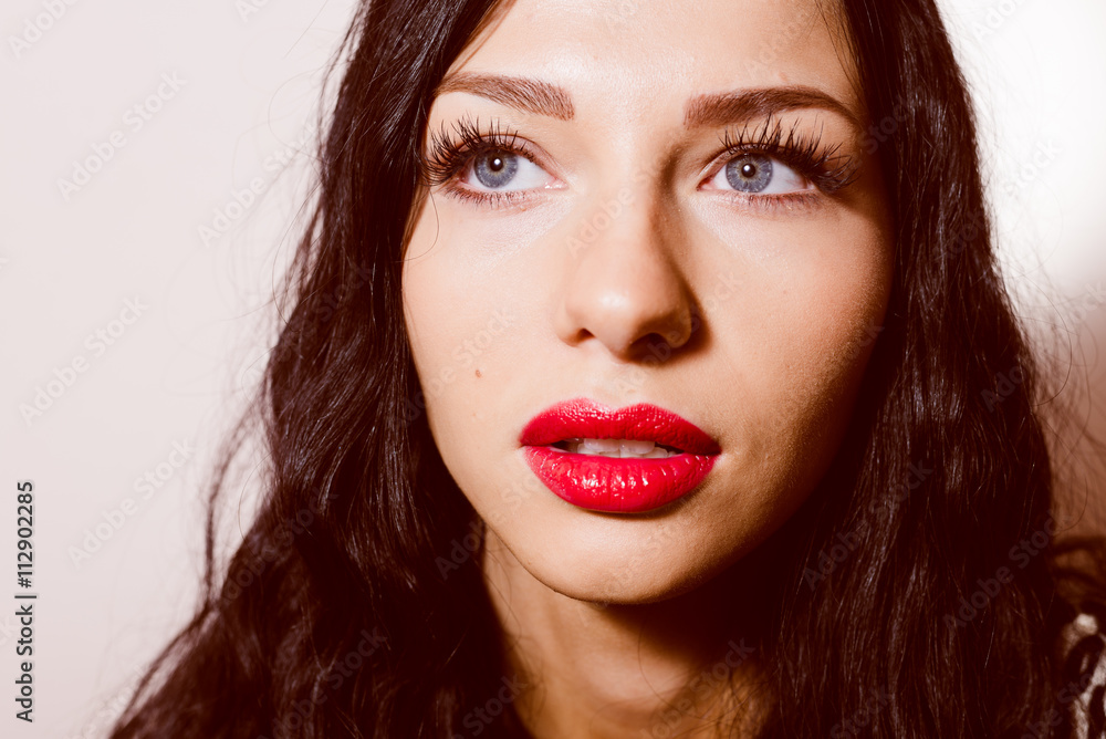 closeup portrait of beautiful sexy young lady with blue eyes and red lipstick having fun sensually looking at camera on light copy space background