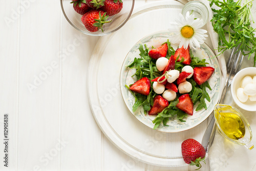 Fresh salad with strawberry, arugula and mozzarella on white plate