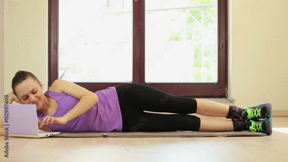 Beautiful girl doing exercises with rubber tape and working at a laptop Beautiful girl doing exercises with rubber tape and working at a laptop