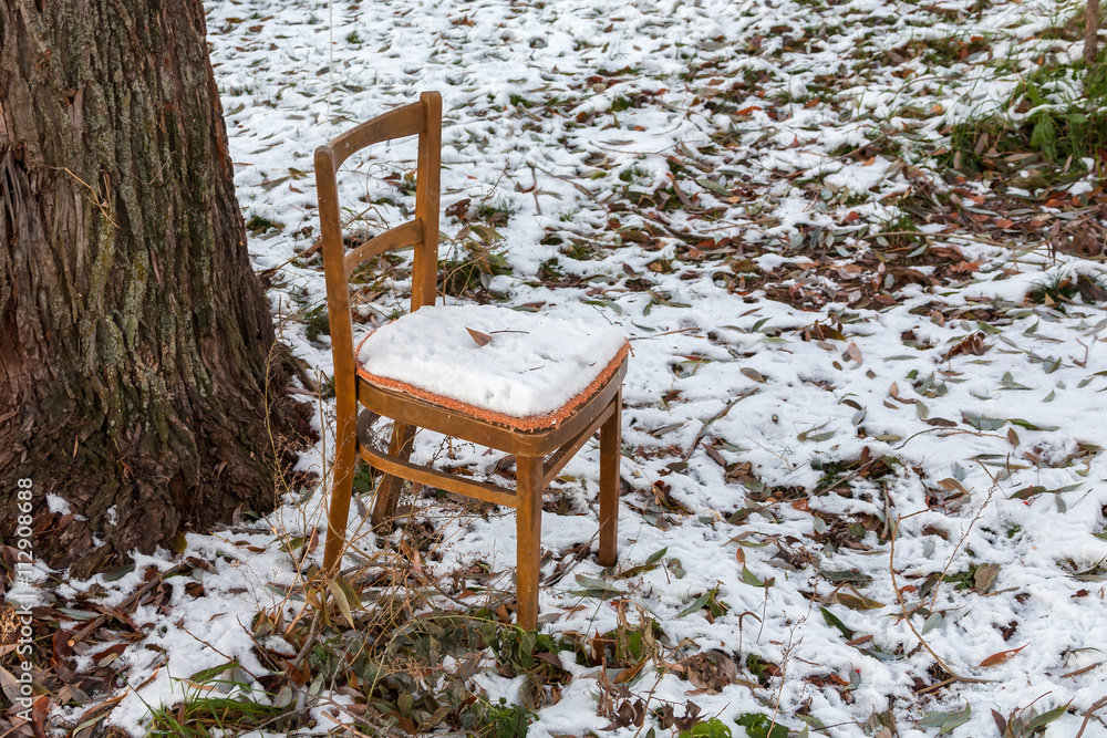 The brown chair forgotten outdoors at a tree under a snow layer