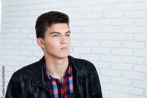 Handsome young man in casual clothes, standing against white brick wall