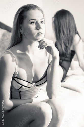 black and white picture of 2 gorgeous sexy pinup girlfriends sitting together in bed on light copyspace background