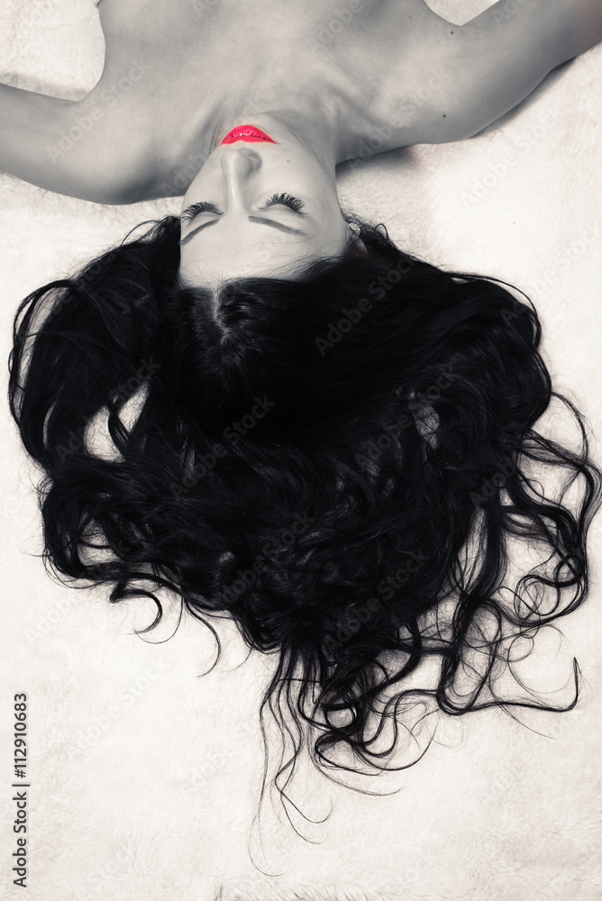 Fototapeta premium black and white portrait of beautiful young sexual glamor lady with red lips in excellent shape having fun relaxing lying on a white bed dreaming with eyes closed on light copy space background