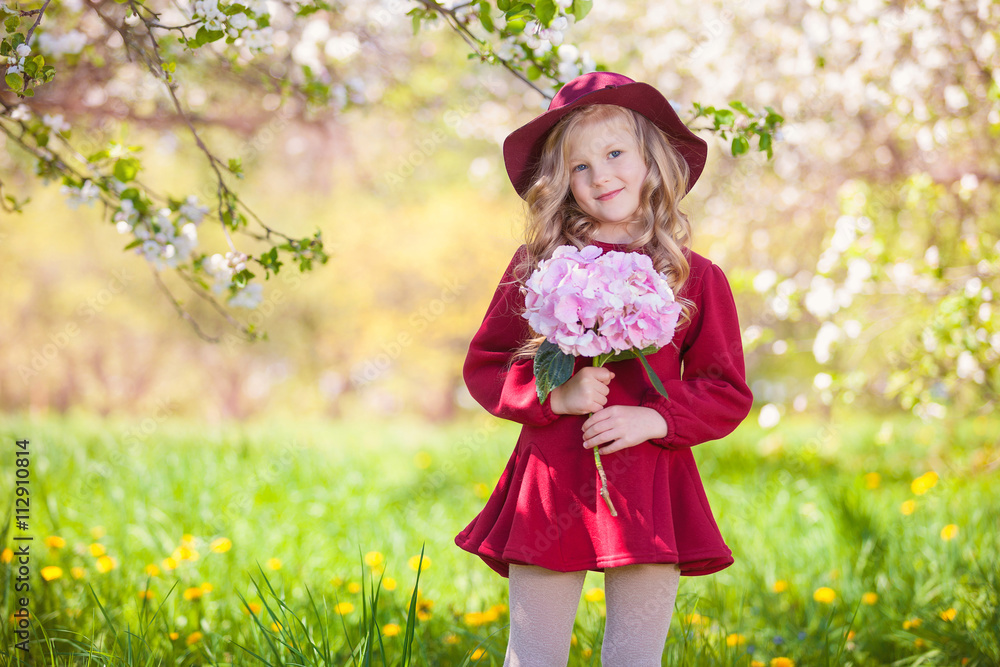 Beautiful little blonde girl in hat and burgundy dress. In her hand bouquet. Summer sunny day, lots of greenery and flowers Beautiful little blonde girl in hat and burgundy dress. In her hand bouquet. Summer sunny day, lots of greenery and flowers