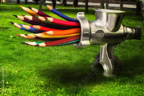 Photo merge - meat grinder grinds colored pencils on a green lawn.