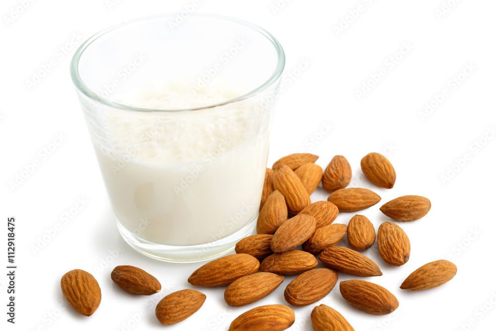 Pile of whole almonds next to glass of almond milk on white. Pile of whole almonds next to glass of almond milk on white.