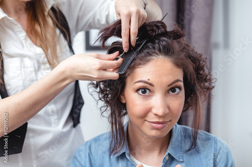 Hair stylist making ringlets to a happy brunette woman. Hairdress
