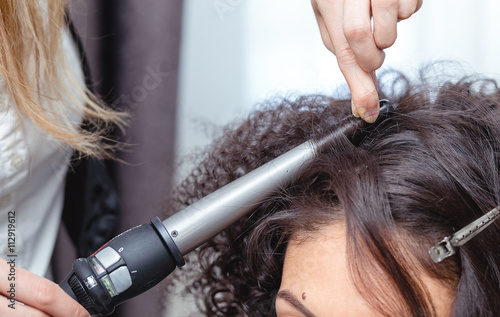 Close-up of a woman hairdresser making curls at long brown hair