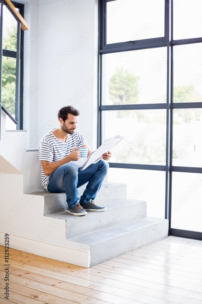 Man on steps having cup of coffee while reading newspaper