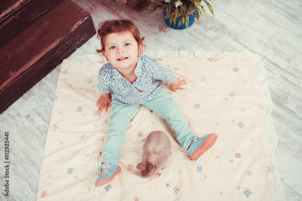 Naklejka premium The little red-haired girl playing with rabbit in the room. The concept of happiness, joy and family values