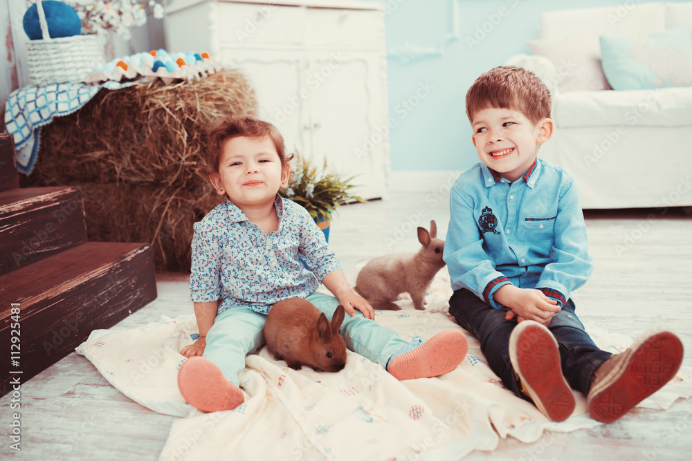 Young children playing with a rabbit in the room. The concept of happiness, joy and family values Young children playing with a rabbit in the room. The concept of happiness, joy and family values