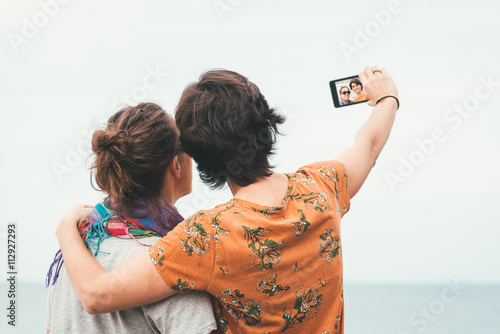 Two young women friends taking a selfie by the sea on summer. Cheerful firiends enjoying sunny day by the sea. photo