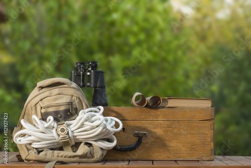 Old travel backpack, safety rope, old wooden suitcase, binoculars, book and old map outdoor shot. Travel kit