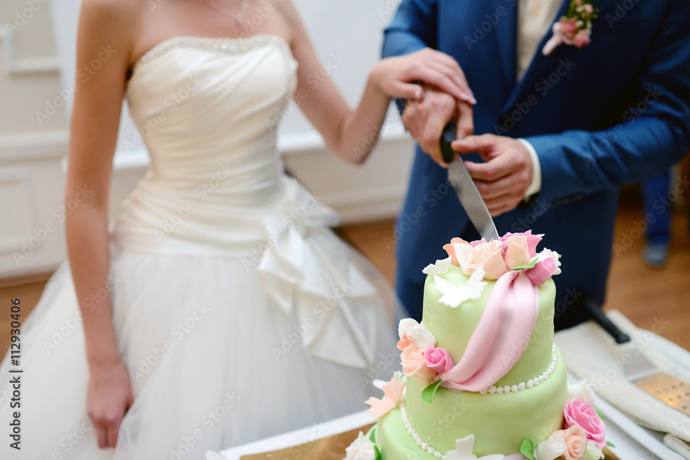 Beauty bride and handsome groom are cutting a wedding cake. Couple in the restaurant with colorful pie. Beautiful model girl in white dress. Man in suit. Female and male portrait. Cute lady and guy Beauty bride and handsome groom are cutting a wedding cake. Couple in the restaurant with colorful pie. Beautiful model girl in white dress. Man in suit. Female and male portrait. Cute lady and guy