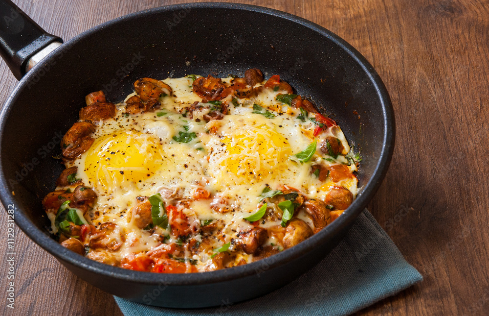 fried eggs with vegetables, mushrooms and cheese in a frying pan on wooden table fried eggs with vegetables, mushrooms and cheese in a frying pan on wooden table