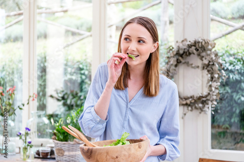 Woman eating salad leaves looking away