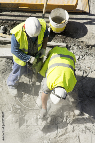 construction worker cutting tiles with electric grinder for repairing sidewalks in city