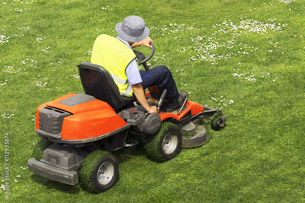 Fototapeta premium pracownik komunalny gminy z kosiarką do trawy, kosiarka jezdna, w parku miejskim