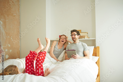 Mid adult couple having lie in whilst daughter falls back on bed photo