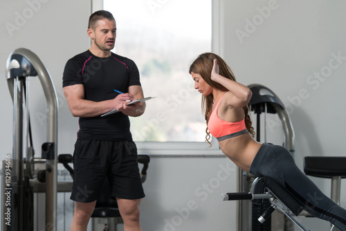Trainer Writing On Clipboard While Woman Training Back