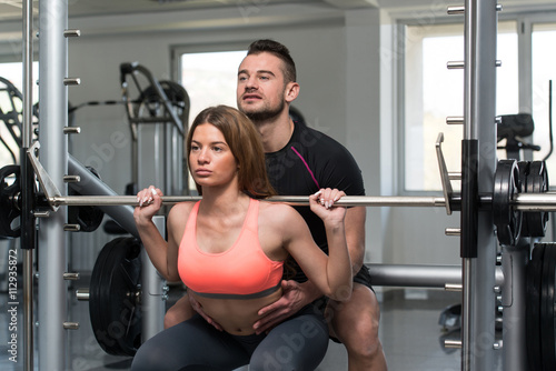 Gym Coach Helping Woman On Barbell Squat