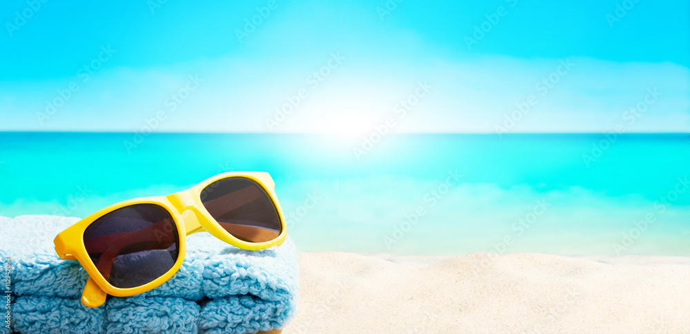 Colorful summer image. Yellow sunglasses with blue towel on beautiful beach resort. Copy space with sunlight. 