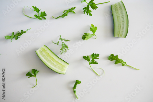 Green pattern made of cucumber, rucola, parsley and dill on the white table. Top view
